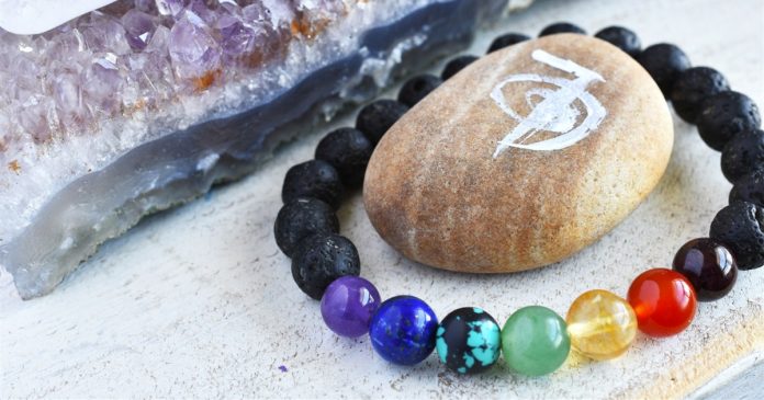 A bracelet of black and colored beads rests beside amethyst and a stone painted with an Om symbol.