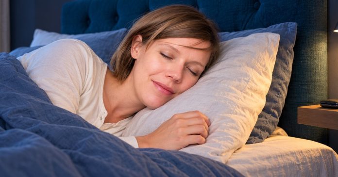 Dreamwalking restful sleep A woman resting on her side beneath blue bedding, with a phone on a bedside shelf.