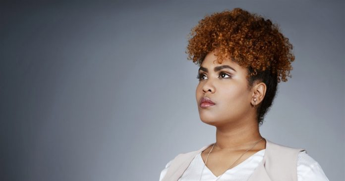 Soul guidance reflection A woman with short copper curls looking thoughtfully to the side against a gray background.