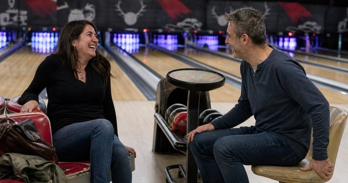 Soulmate connection shared laughter Two adults laughing together beside the lanes at a bowling alley.